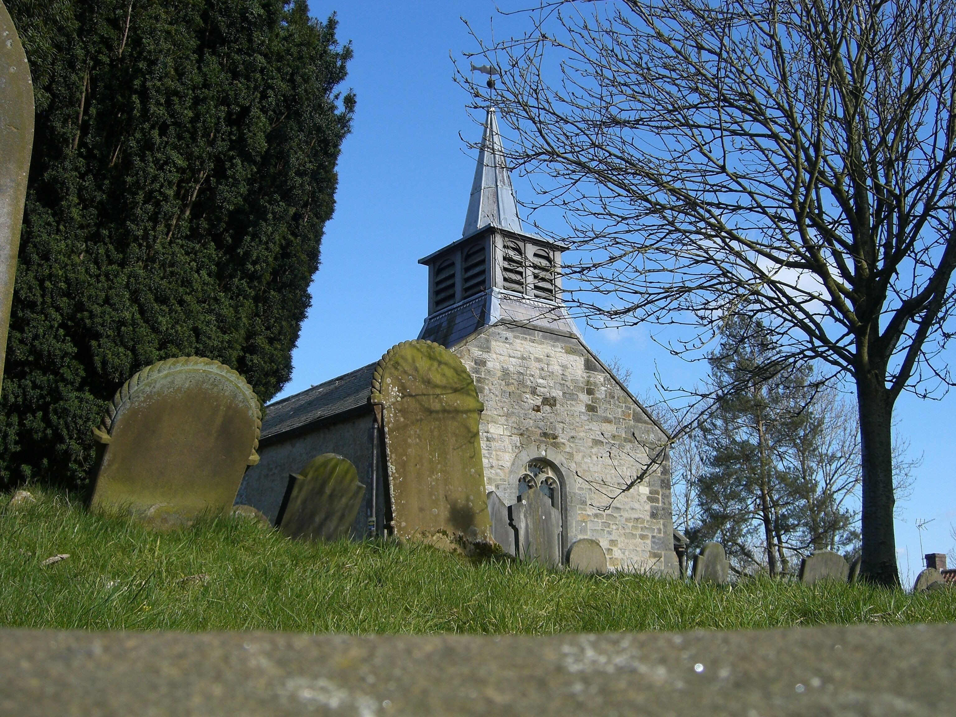 A church with a steeple, surrounded by gravestones and trees.