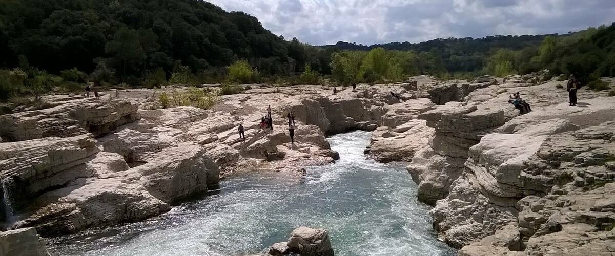 A rocky river with people standing on the rocks and a waterfall.