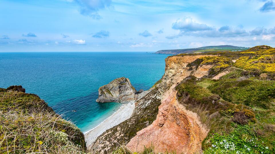 A coastal landscape with a rocky cliff, beach, and ocean.