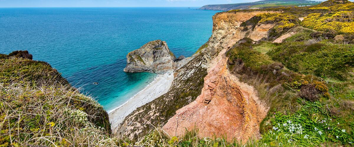A coastal landscape with a rocky cliff, beach, and ocean.