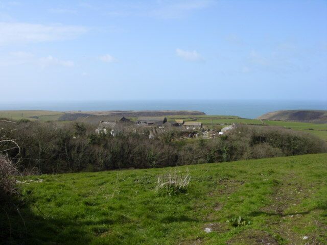 From Upton to Trecarne Farm Upton (behind photographer) is a farm converted to holiday cottages and also performs civil marriages. Trecarne Farm (centre) still has its dairy herd and its road runs in from the left along a stream at the bottom of the wooded valley. These farms are south of Trebarwith Strand and in Tintagel parish.