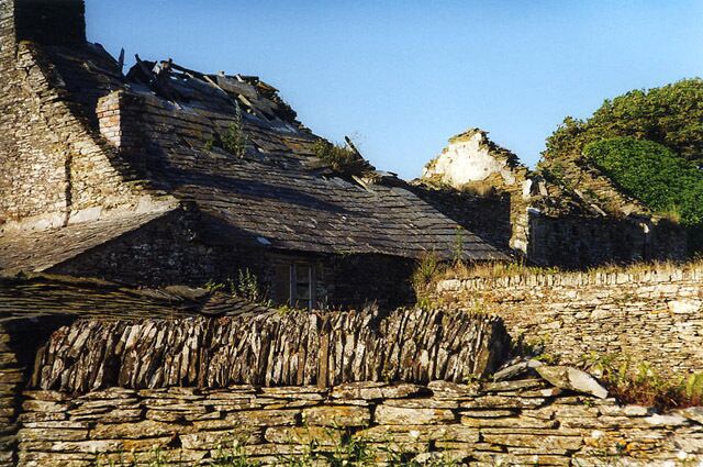 A stone structure with a sloped roof, surrounded by stone walls and vegetation.