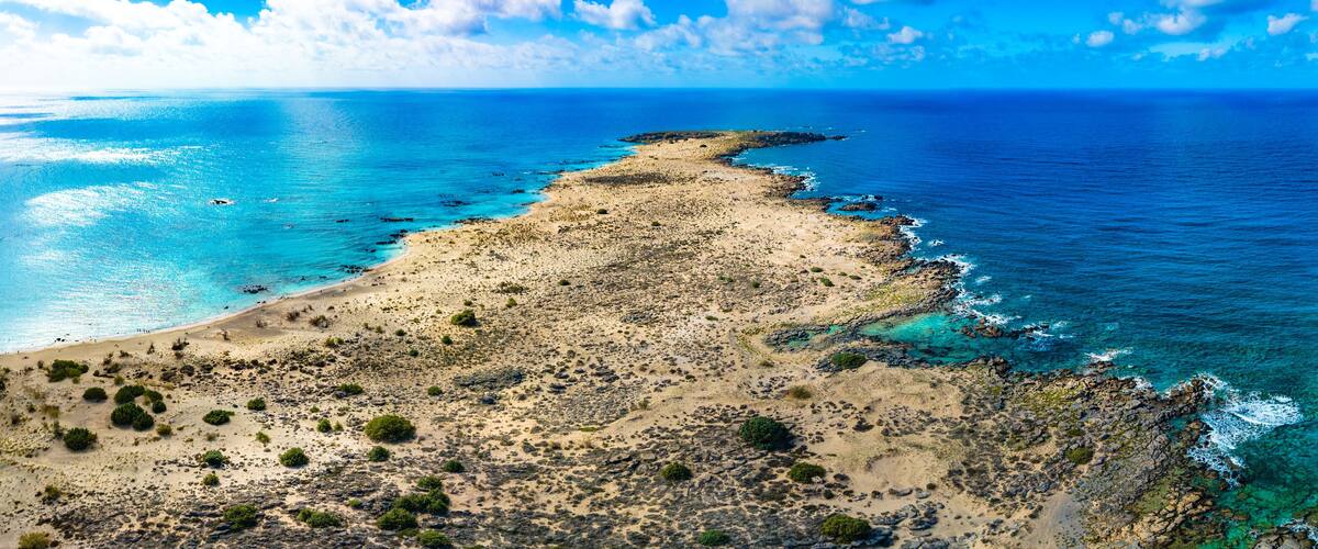A coastal landscape with a sandy beach, rocky outcrops, and clear blue waters.