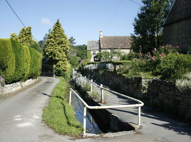 A narrow rural road with a stone wall on one side and a metal guardrail on the other.