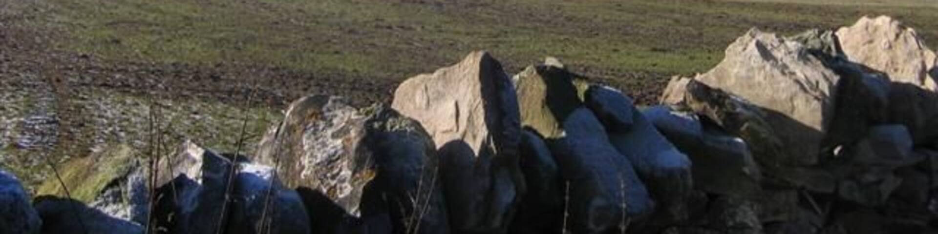 A stone wall, rolling hills, and distant mountains.
