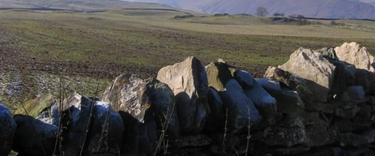 A stone wall, rolling hills, and distant mountains.