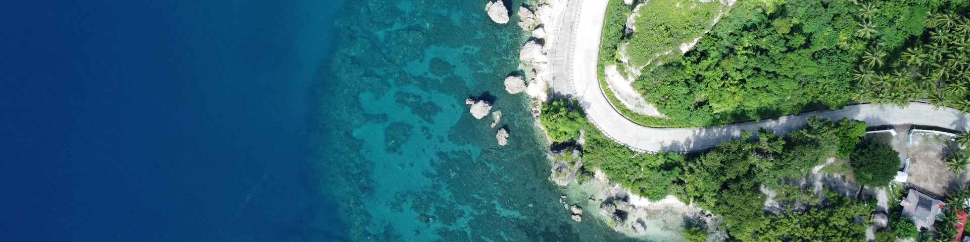 A coastal road winding through a lush green landscape with clear blue waters and rocky outcrops.