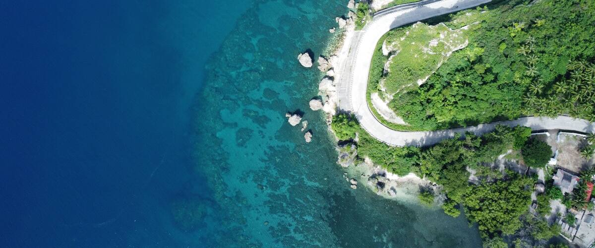 A coastal road winding through a lush green landscape with clear blue waters and rocky outcrops.