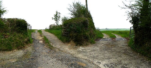 A rural dirt road leading to a gated entrance surrounded by vegetation.