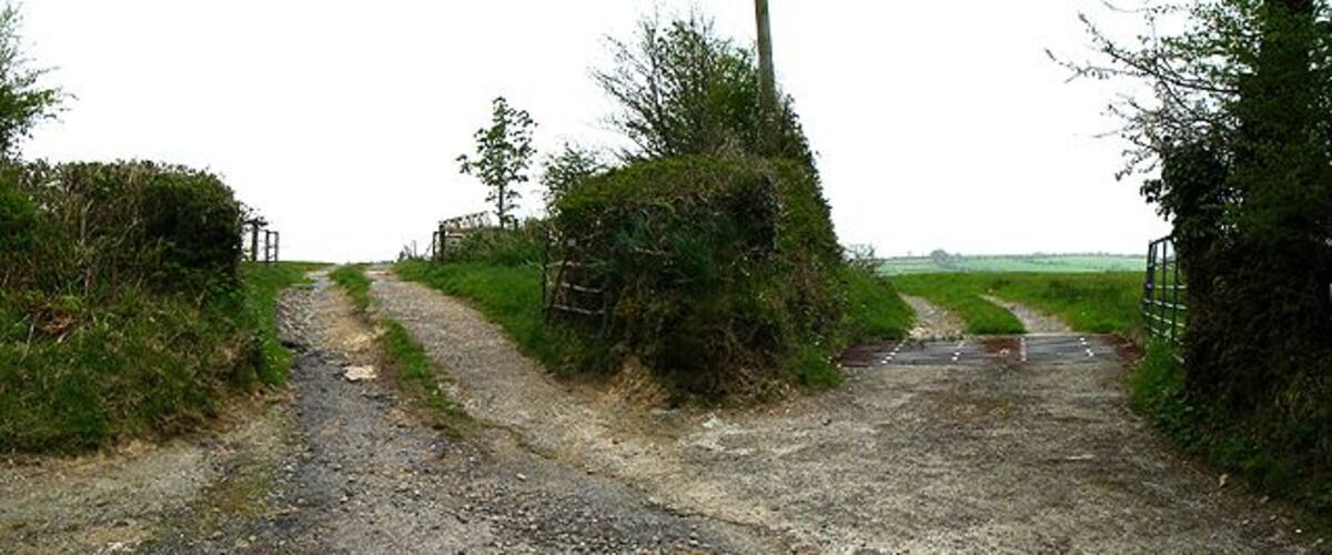 A rural dirt road leading to a gated entrance surrounded by vegetation.