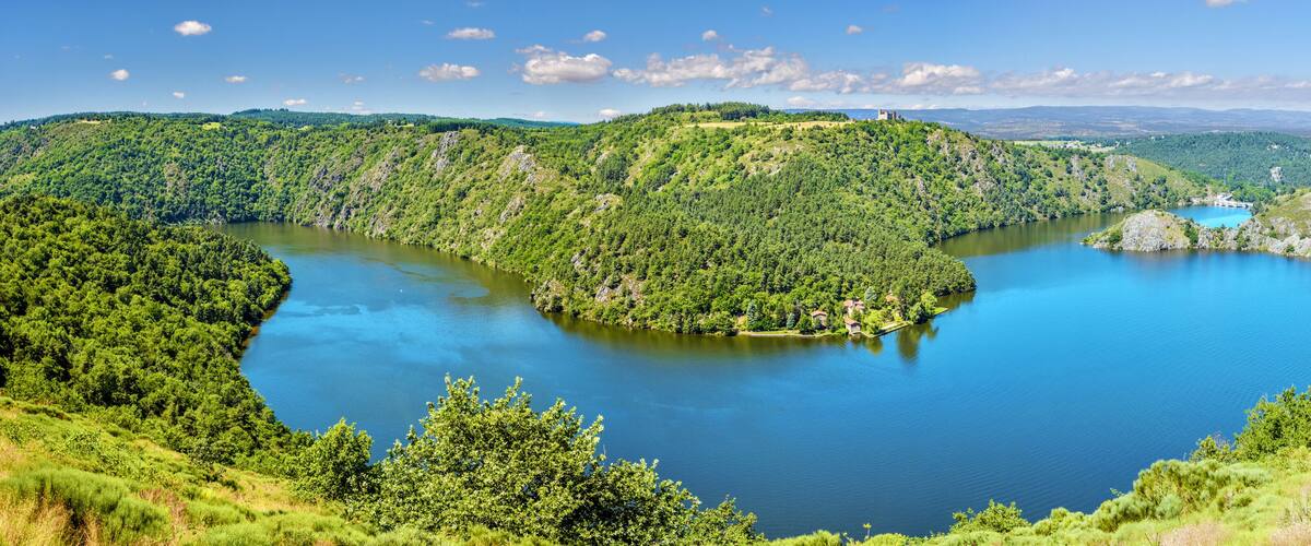 A lake surrounded by lush green hills and a castle on a hill.