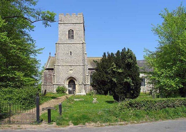 A stone church with a bell tower, surrounded by greenery and a fence.