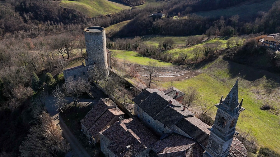 Un pueblo histórico con edificios de piedra, una torre de iglesia y campos en terrazas.