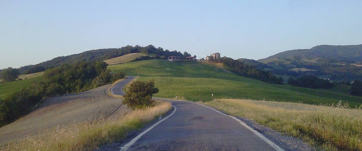 A winding road through rolling hills with a small building on a hill in the distance.