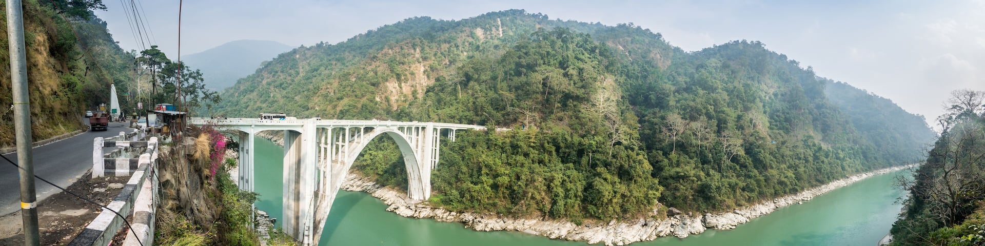 A white bridge over a green river, surrounded by forested hills.