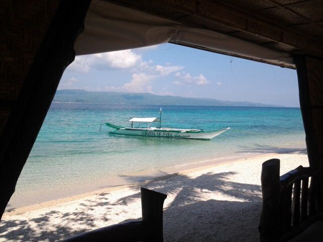 A boat on turquoise water, a sandy beach, and a mountainous landscape in the distance.