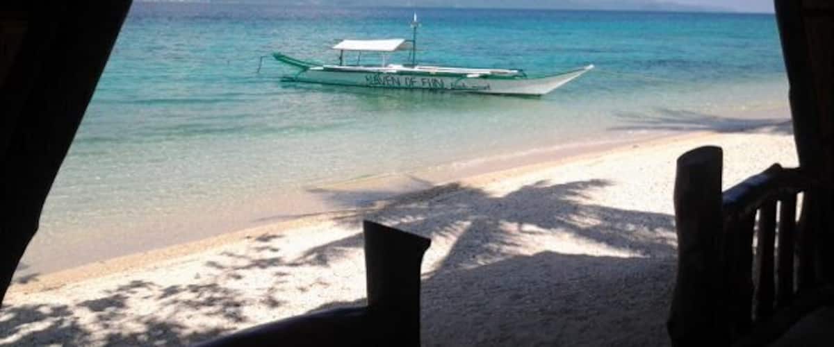 A boat on turquoise water, a sandy beach, and a mountainous landscape in the distance.