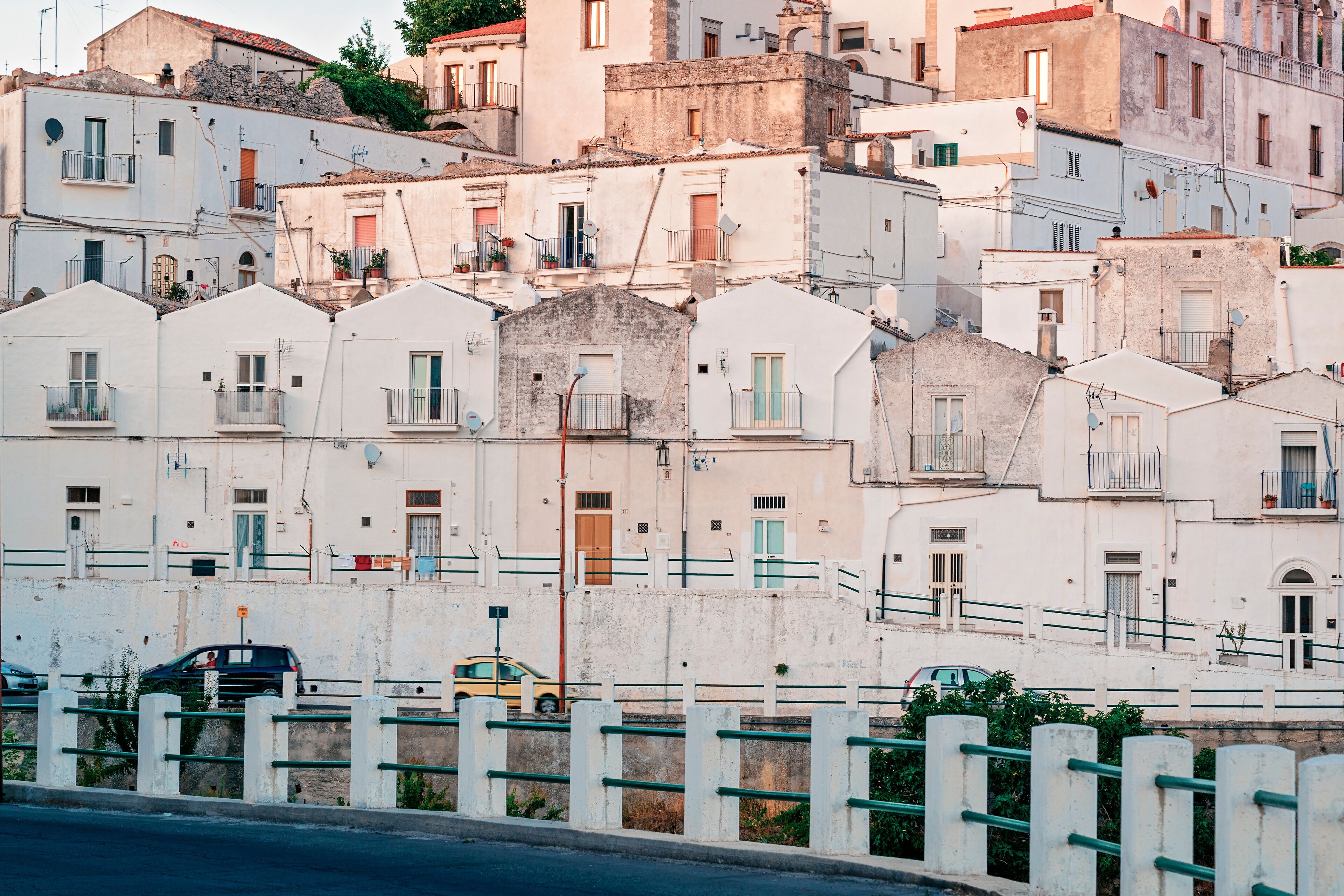 A row of white buildings with balconies and a yellow car parked in front.