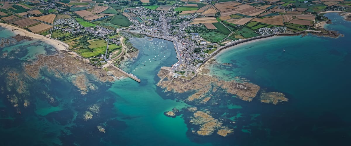 An aerial view of a coastal town with a beach, farmland, and rocky outcrops.