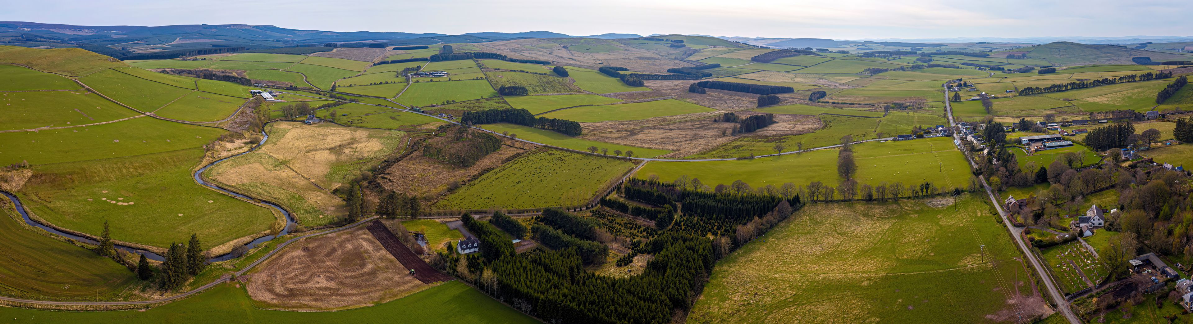 Paisaje rural con colinas onduladas, campos, un río y edificios dispersos.