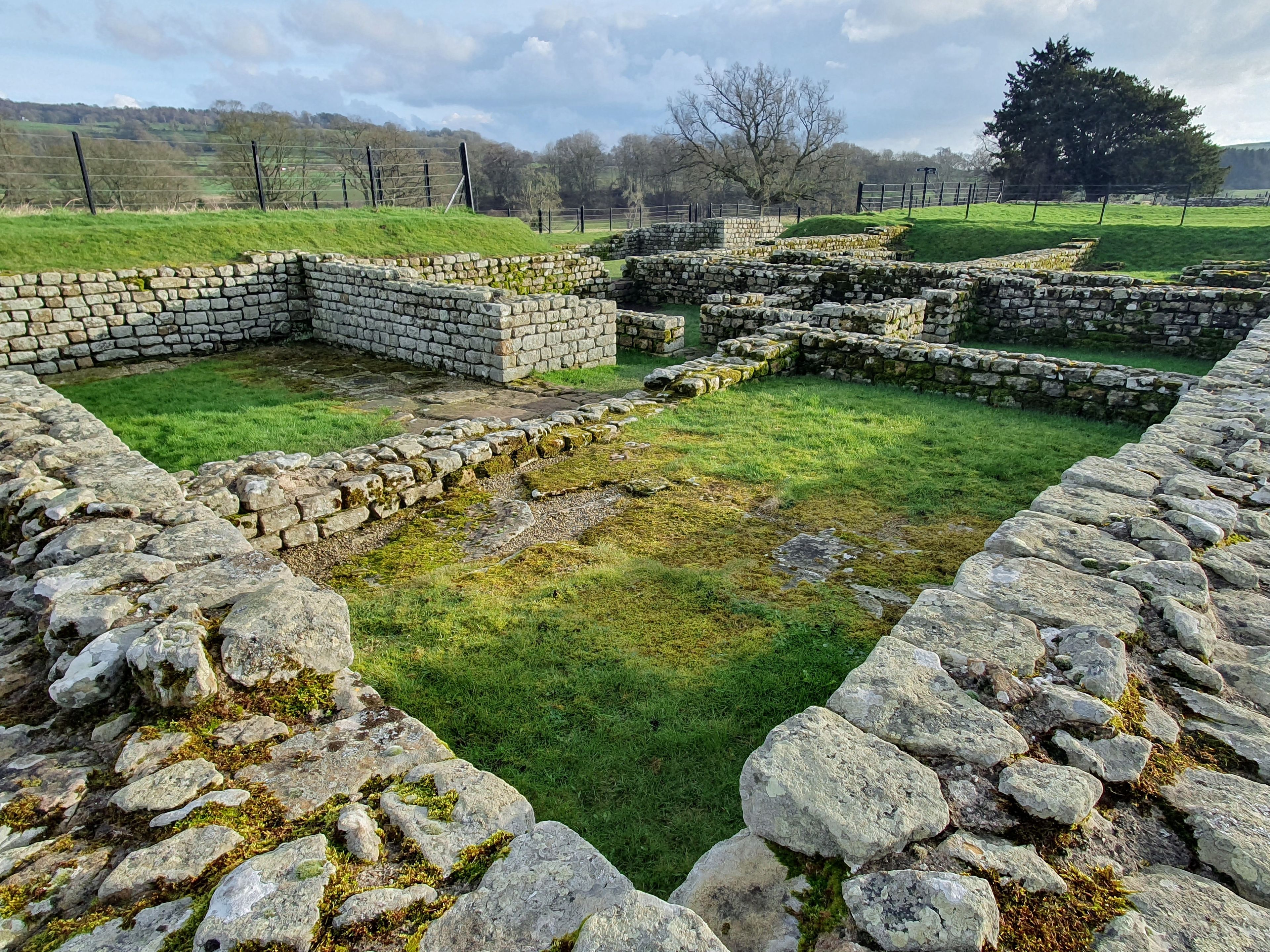 Ruinas de piedra antiguas con un campo cubierto de hierba y muros de piedra.