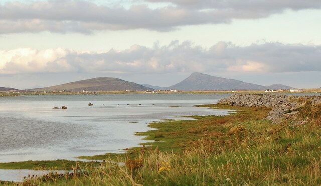 A coastal landscape with a body of water, grassy areas, and distant hills.