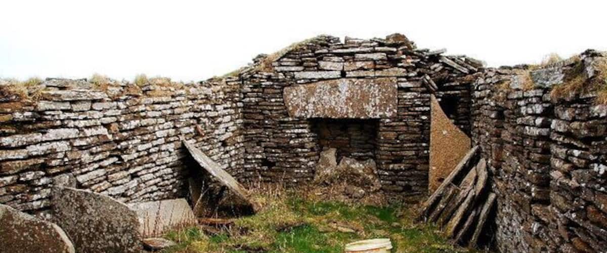 A stone structure with a central opening, surrounded by grass and scattered stones.