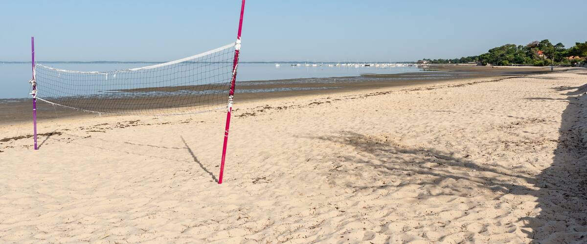 A beach volleyball net on a sandy beach with a clear sky.