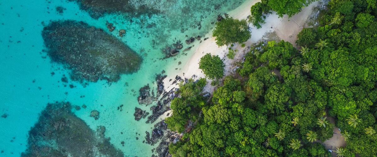An aerial view of a tropical island with clear turquoise waters, rocky outcrops, and dense green vegetation.