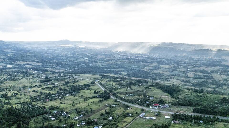 An aerial view of a rural landscape with rolling hills, scattered houses, and a winding road.