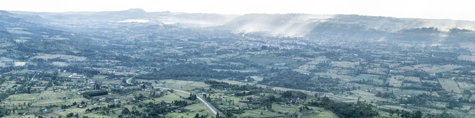 Aerial view of the sprawling green landscape is bisected by a long road under a bright sky, Nairobi, Kenya.