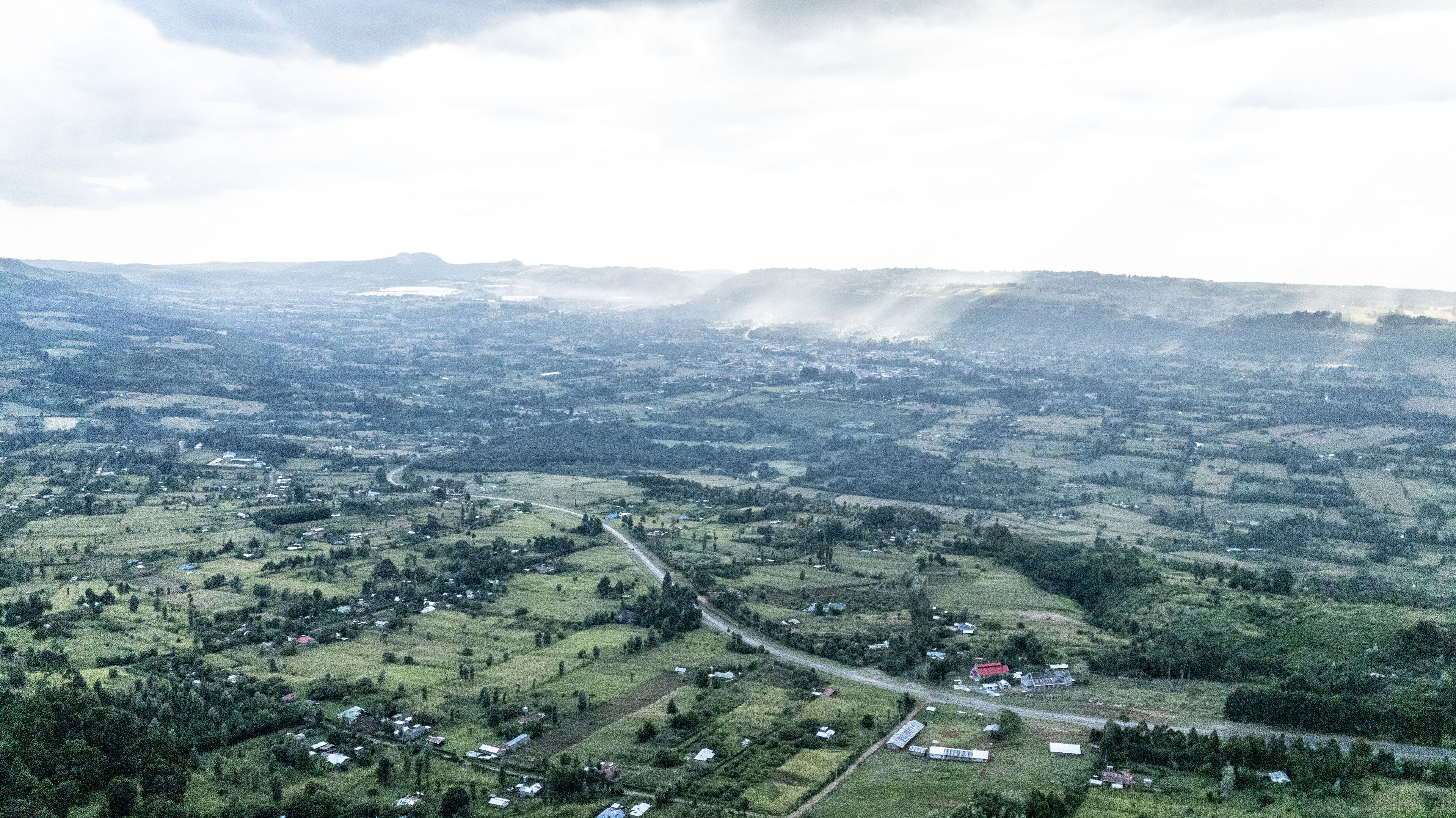 An aerial view of a rural landscape with rolling hills, scattered houses, and a winding road.
