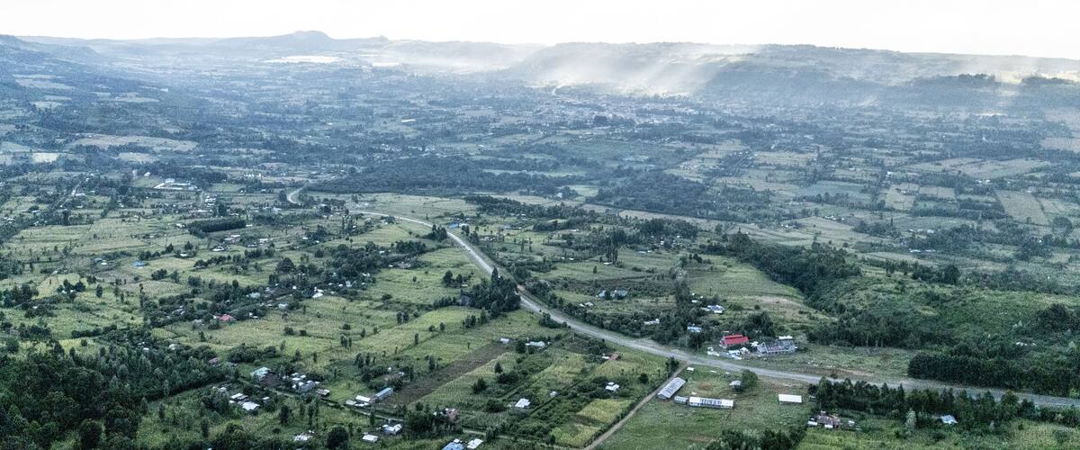 An aerial view of a rural landscape with rolling hills, scattered houses, and a winding road.