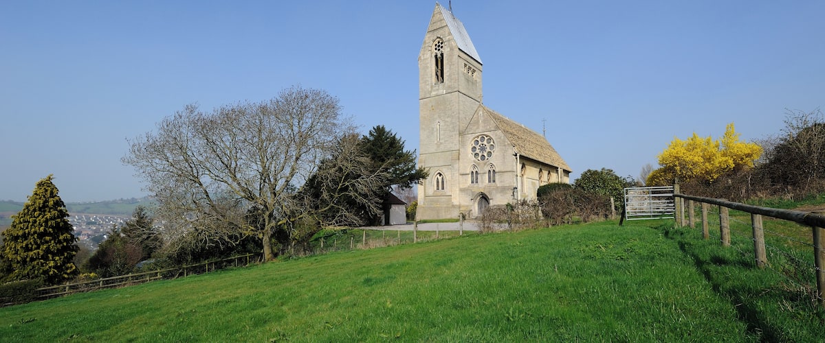 A church with a tall tower, surrounded by a grassy field and trees.