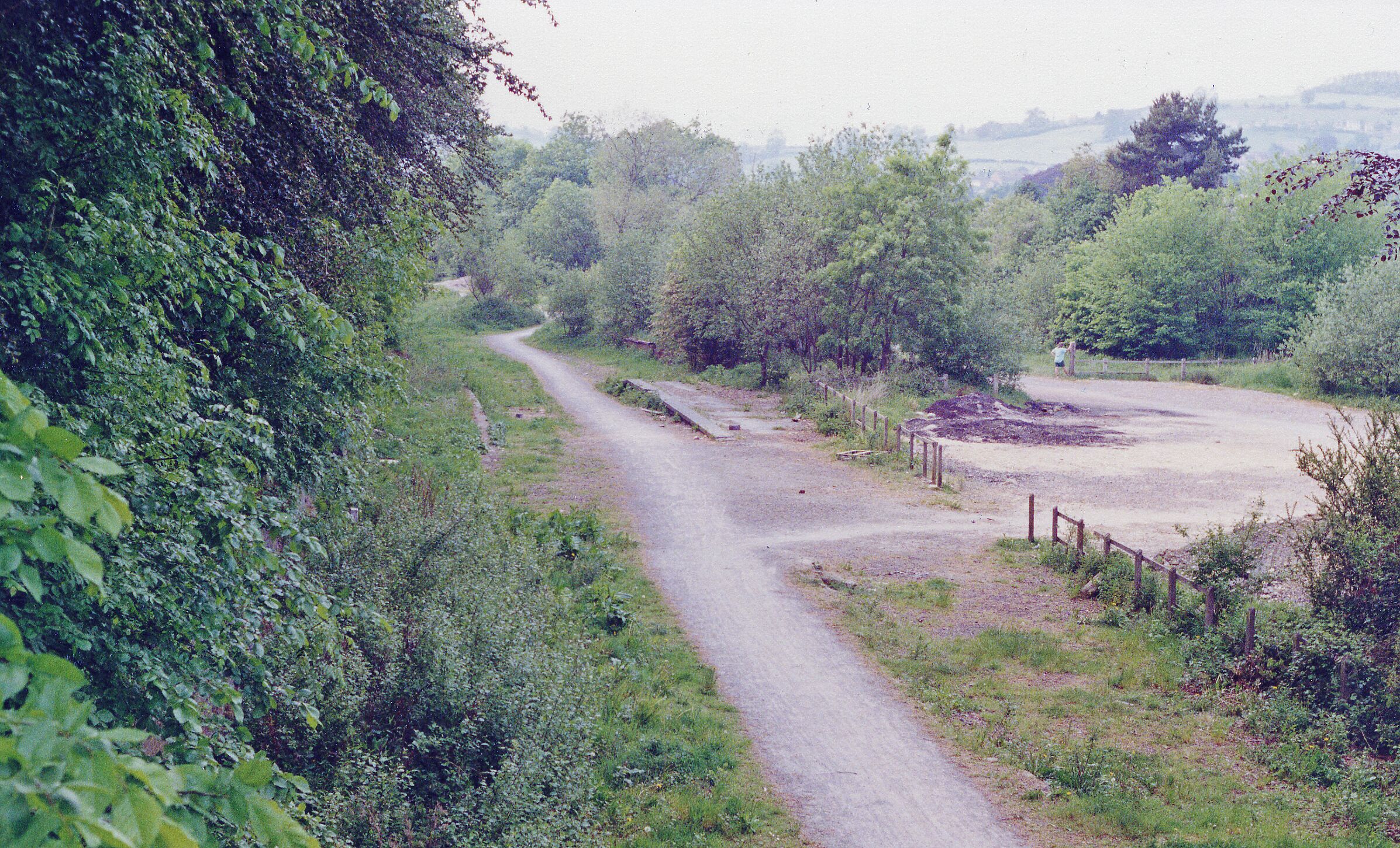 A rural dirt road winding through a wooded area with a fenced field on the right.
