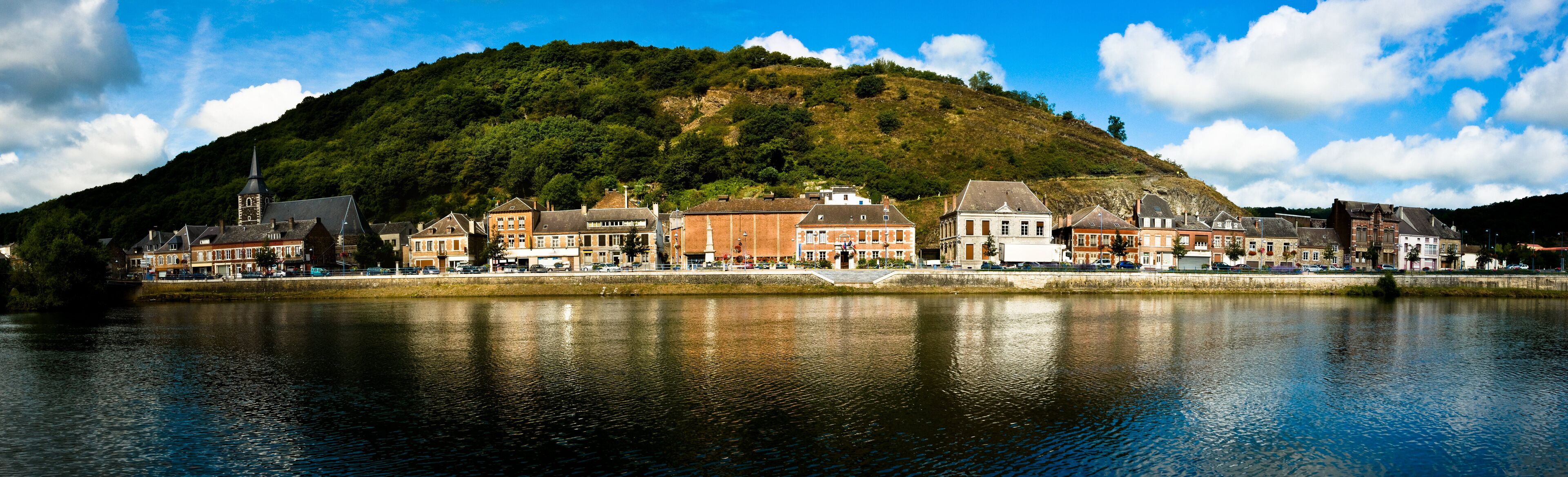 A riverside town with historic buildings, a church, and a hill in the background.