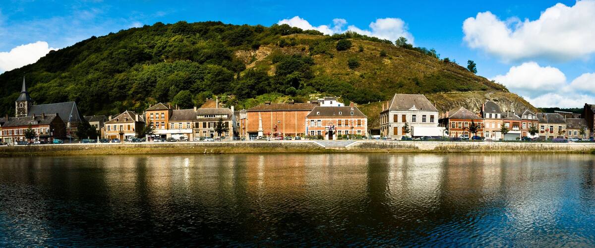 A riverside town with historic buildings, a church, and a hill in the background.