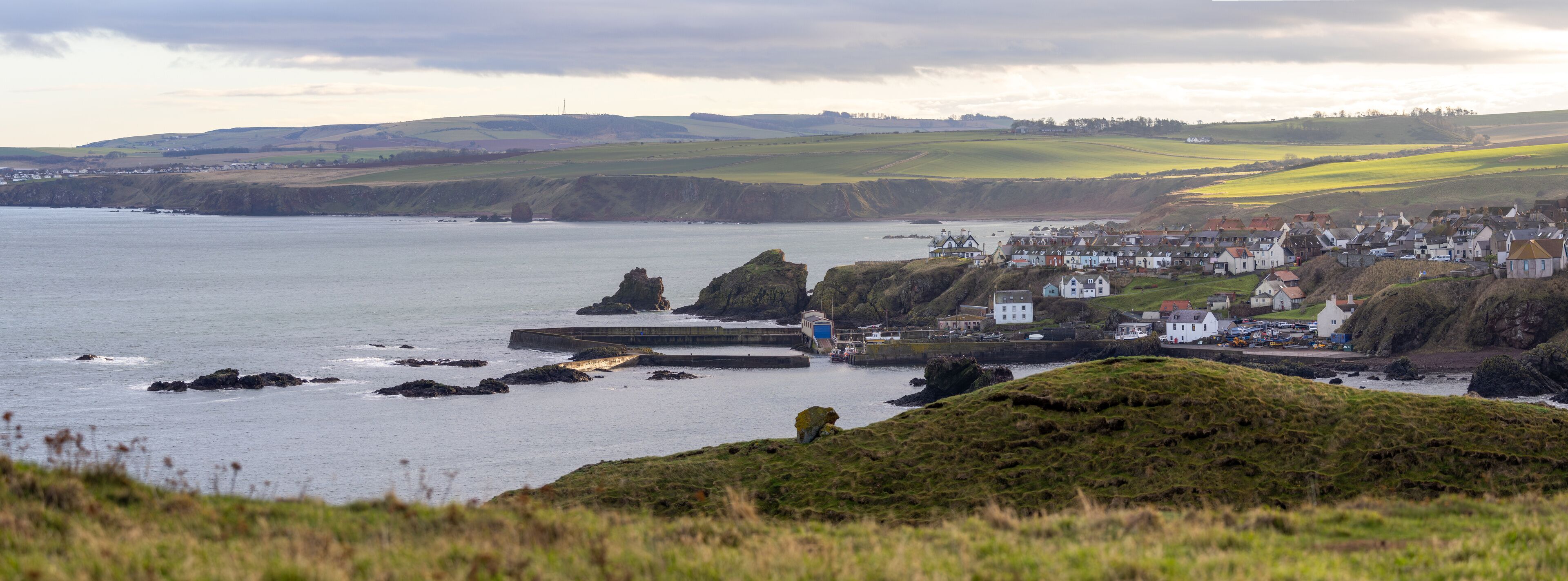 Panoramic view of St Abbs in Scotland with cliffs, harbor, and sea under cloudy light.