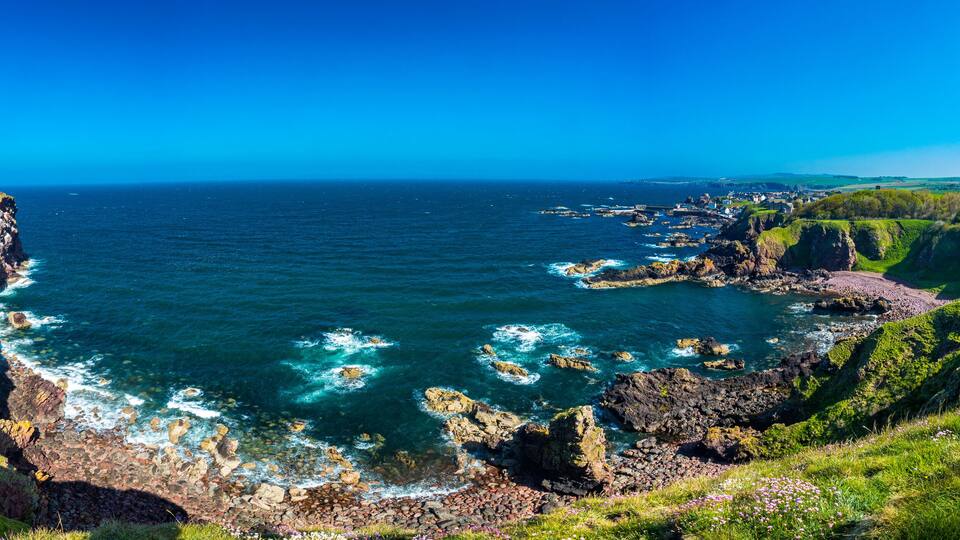 A coastal landscape with cliffs, rocky shores, and a clear blue sea.