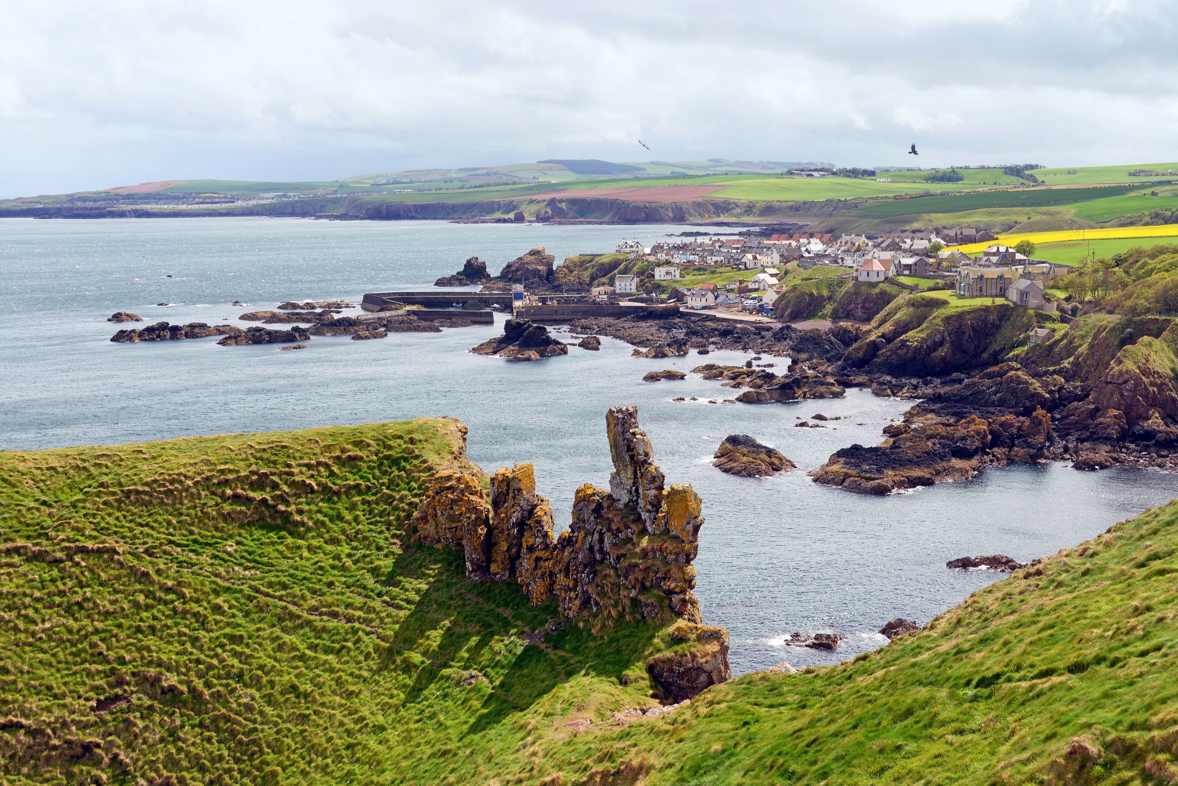 A coastal town with rocky outcrops, green hills, and a body of water.