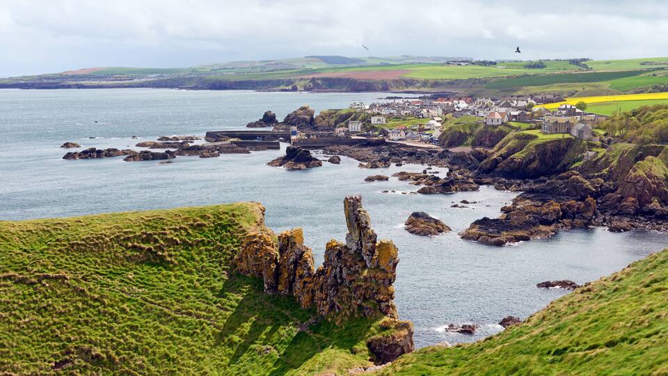 A coastal town with rocky outcrops, green hills, and a body of water.