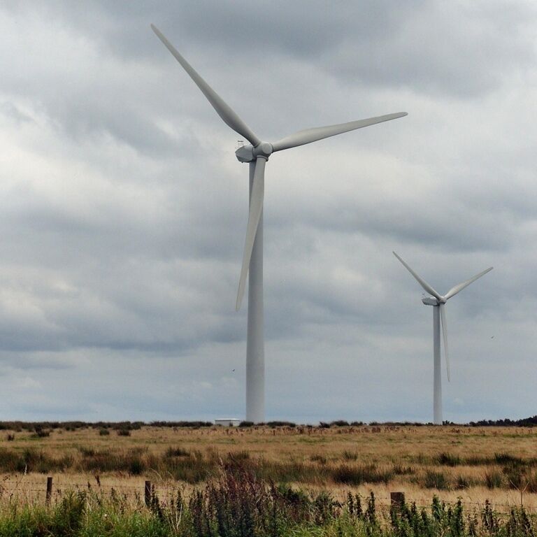 Two wind turbines in a grassy field under a cloudy sky.
