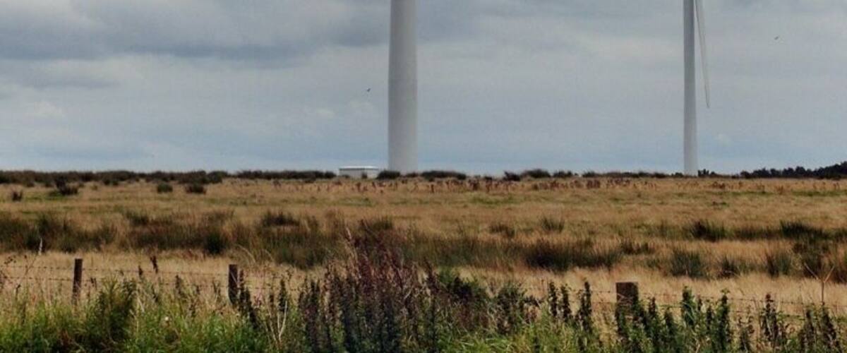 Two wind turbines in a grassy field under a cloudy sky.