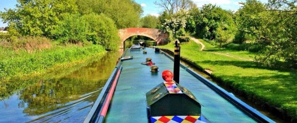 A narrow waterway with a boat, greenery, and a brick bridge.
