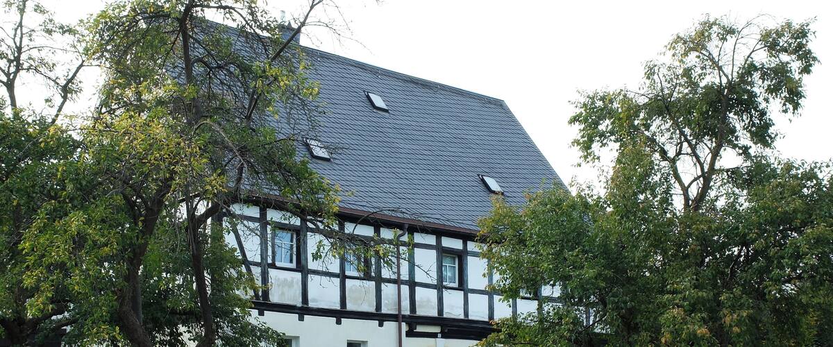 A white house with a dark roof, surrounded by lush greenery and trees.