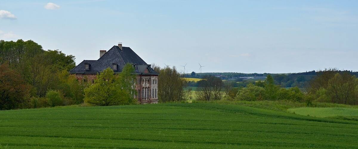 A large green field with a historic building and wind turbines in the background.