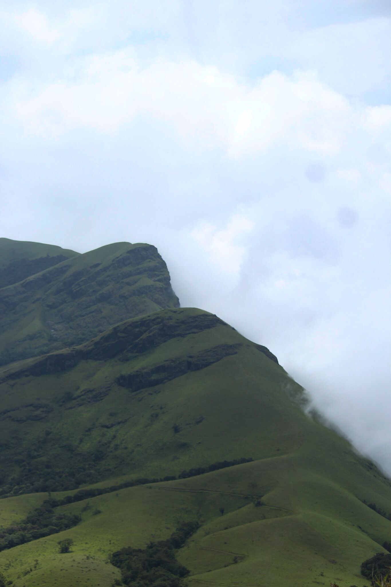 Rolling green hills with a mountain in the background partially obscured by clouds.