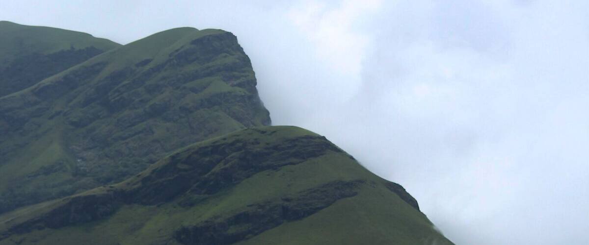 Rolling green hills with a mountain in the background partially obscured by clouds.