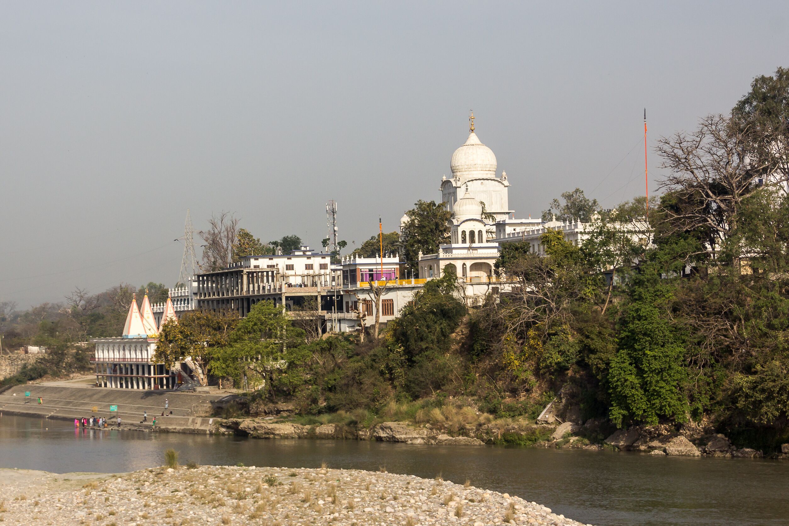 A river with a temple on a hill, surrounded by trees and buildings.