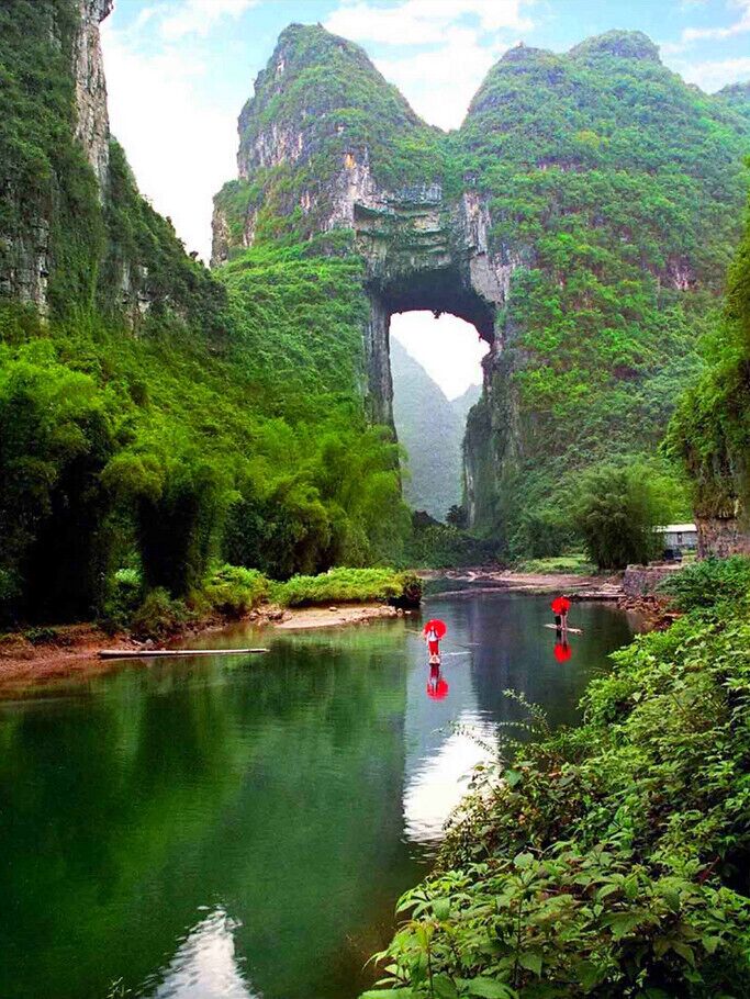 A river with a natural arch formation surrounded by lush greenery.